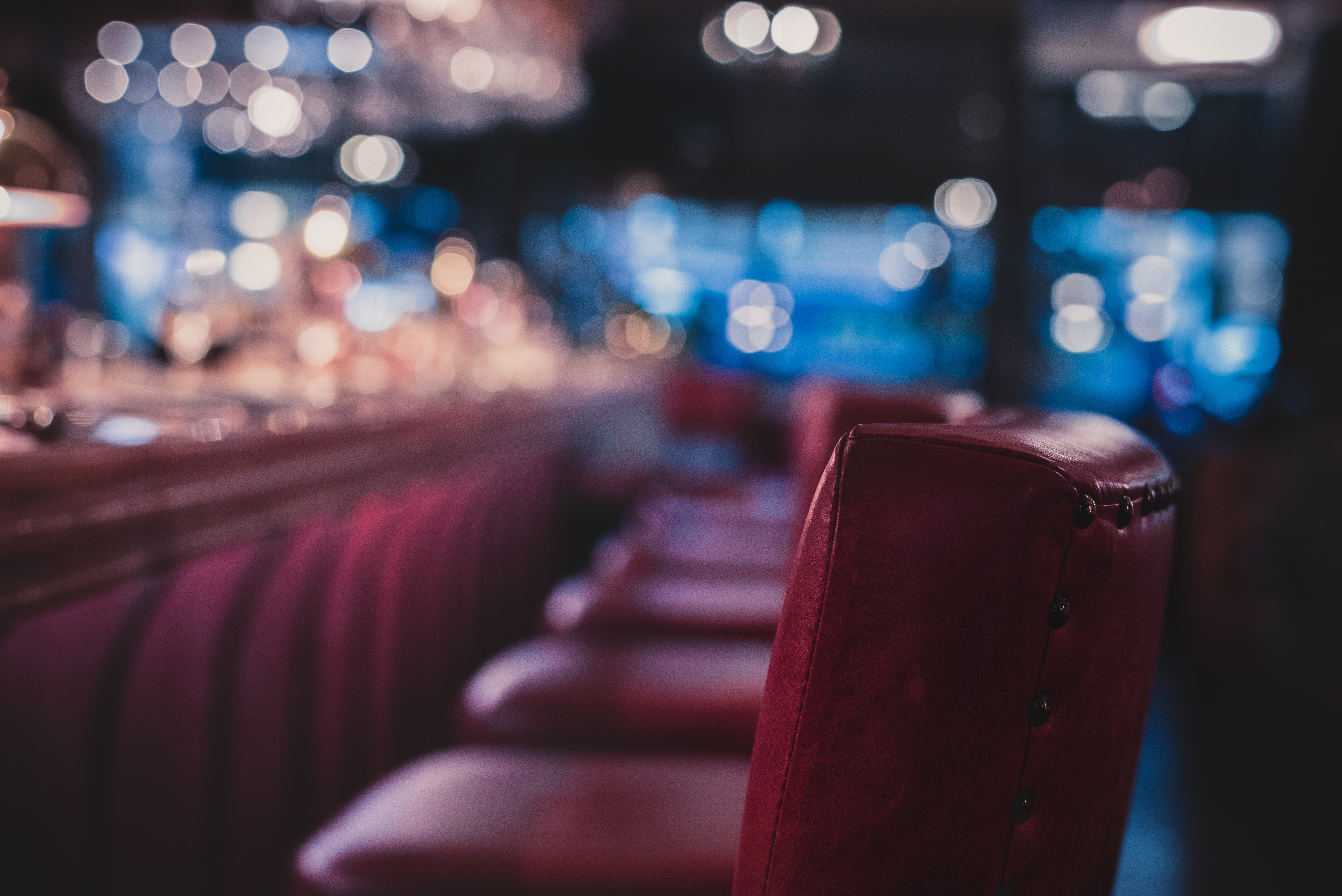 A view straight down the line of red-leather chairs at a dim bar, with most everything except the nearest seat out of focus.