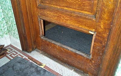 An old wooden front door with the lower panel entirely removed, leaving a hole big enough to wriggle through.